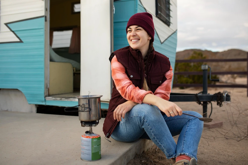 a girl sitting infront of RV and making coffee with portable stove