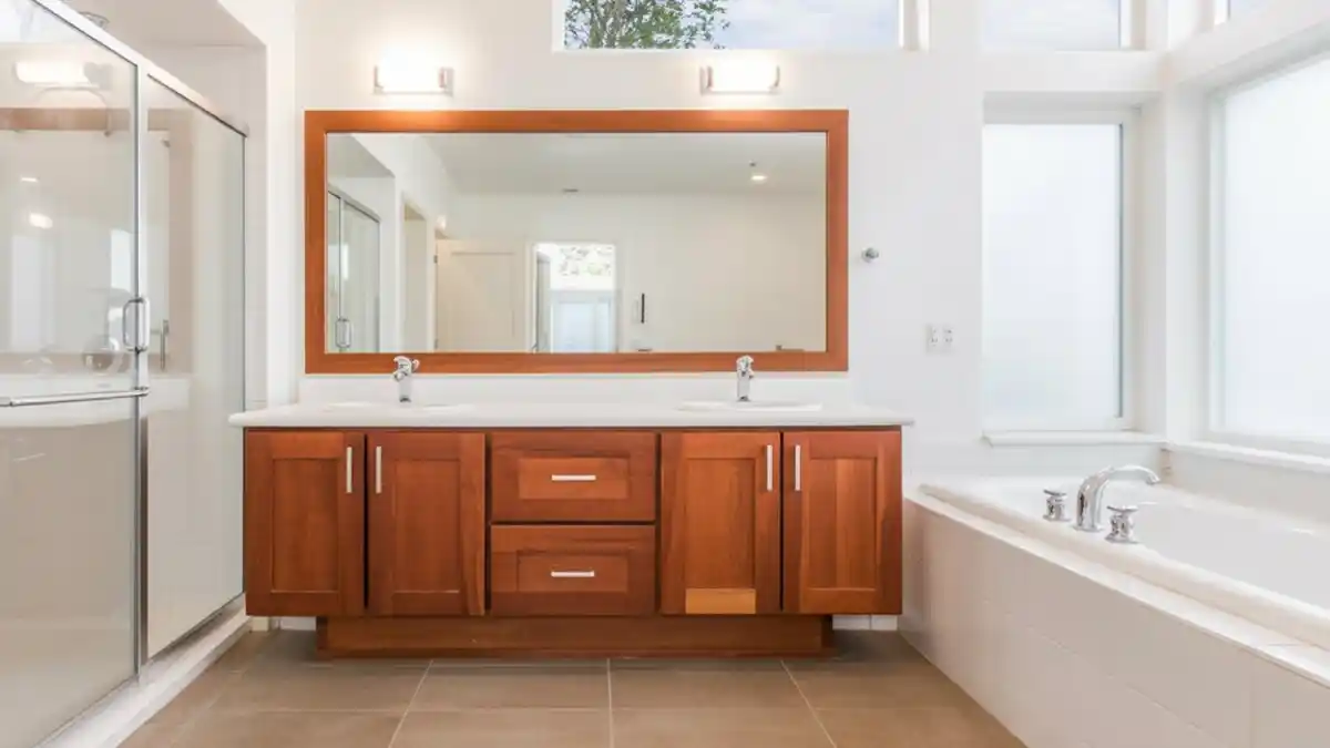 Rich taupe hues redefine the neutral palette, offering a grounding, earthy alternative to the stark white cabinets of the past decade. Saturation is key here; a full-coverage paint in "Mushroom" or "Warm Putty" completely masks the grain of dated oak, instantly modernizing the silhouette while retaining a cozy, organic feel. Swap standard white for a deep, comforting earth tone.Vertical wood slats introduce essential rhythm, providing a textural counterpoint to the smooth, painted finish of the vanity. Installing fluted paneling or beadboard as a wainscoting breaks up the drywall and mimics the linear details of the cabinetry, creating a high-end, architectural look on a DIY budget. Elevate the vanity wall with tactile, linear texture.Monochromatic framing unifies the design, seen here where the mirror frames are painted to match the vanity exactly. Treating the mirrors as an extension of the cabinetry rather than a separate accessory makes the entire washing station feel like a custom, built-in piece of furniture. Create a seamless, custom look by color-matching accessories.Geometric flooring prevents beige fatigue, injecting a pulse of energy into the room with sharp angles and cool grey tones. Laying a patterned tile contrasts beautifully with the solid blocks of color on the wall and vanity, ensuring the warm neutral theme doesn't feel monotonous or washed out. Use dynamic floor patterns to energize a warm, neutral space.